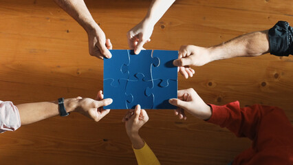 Top down view of skilled business people assemble blue jigsaw puzzle on meeting table. Group of diverse team working together to solve the puzzle. Represented togetherness, cooperative. Convocation.