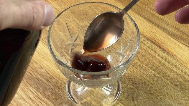 Pouring strawberry jam with whole berries in glass dessert bowl