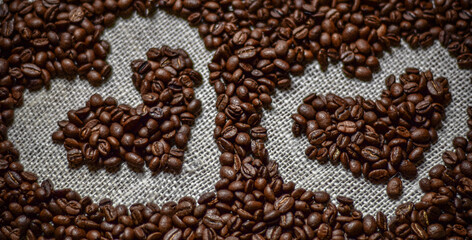 The image shows a close-up of dark, roasted coffee beans. One bean is in focus, highlighting its natural seam. The rest are blurred, creating a rich, textured background.

