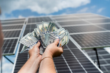 worker with hundred dollar bills as saving money, against  solar station