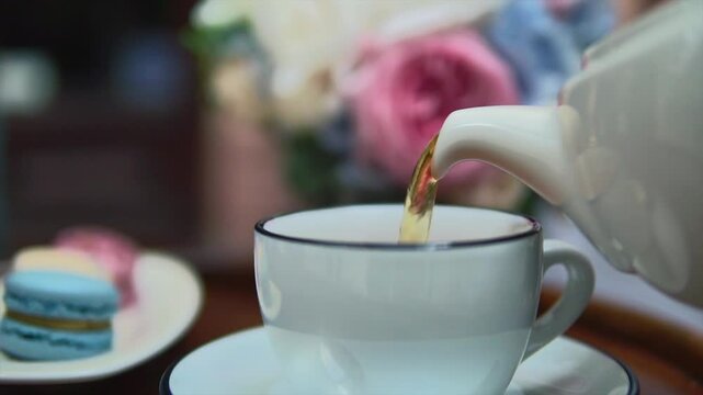 Classy estetique Shot with Bouquet of Flowers and Macarones. Hands pouring black tea from teapot into porcelain cup.