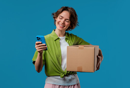 Excited smiling woman, online shopping consumer received cardboard order parcel box, desired purchase. Mobile phone, smartphone mockup with copy space screen for your advertisement