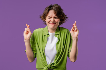 Young woman praying with crossed fingers, violet background. Lady begs someone, satisfy desires,...