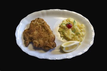 Breaded cutlet with potato salad and lemon on a plate, black background, cutout, Germany, Europe