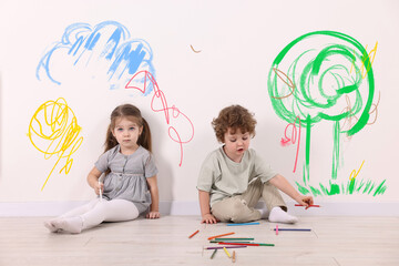 Little children sitting near white wall with drawings