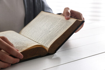 Naklejka premium Man with Bible at white wooden table, closeup