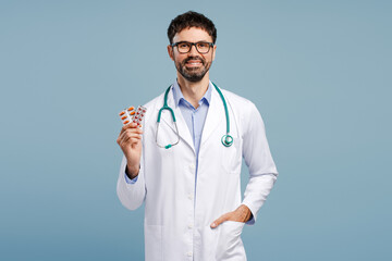 Smiling, positive, professional doctor wearing white coat and stethoscope holding pills