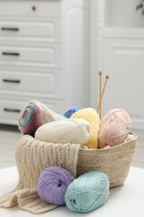Skeins of yarn, knitting sample and needles on white table indoors