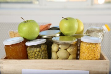 Different food products for donation in wooden crate indoors, closeup