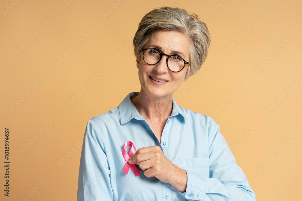 Wall mural Senior woman smiling and showing pink ribbon for breast cancer awareness