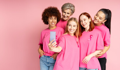 Diverse women taking selfie wearing pink ribbons for breast cancer awareness