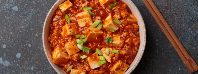 Mapo tofu, a popular Chinese Sichuan dish, served in a bowl and garnished with green onion. Chopsticks are laying next to the bowl
