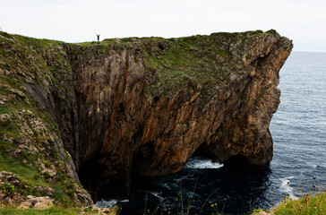 A human figure raises his arms at the top of a steep cliff