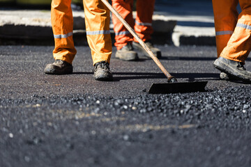 Construction workers in bright orange uniforms working diligently to lay asphalt on a city street during the daytime.