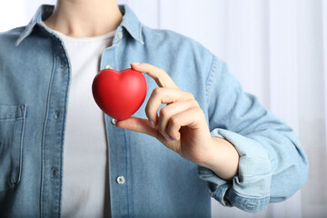 Woman holding red heart on light background, closeup