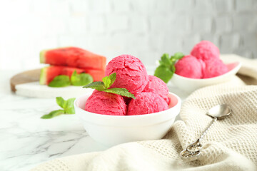 Scoops of tasty watermelon sorbet with mint in bowls and spoon on white marble table