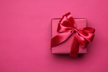 Gift box with bow on pink background, top view. Space for text