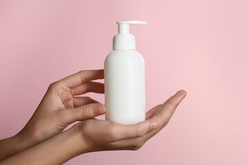 Woman with shampoo bottle on pink background, closeup