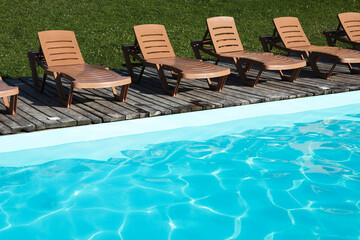 Empty sun loungers on wooden deck near outdoor swimming pool