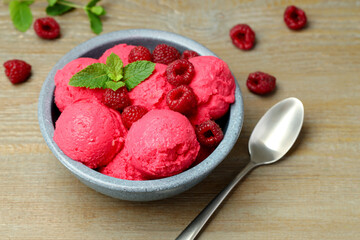 Delicious raspberry sorbet with fresh berries in bowl and spoon on wooden table