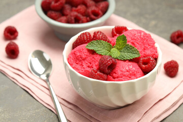 Delicious raspberry sorbet with fresh berries in bowl and spoon on gray textured table, closeup
