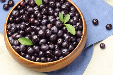 Ripe acai berries and leaves in bowl on table, above view