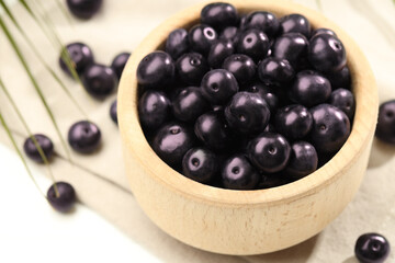 Ripe acai berries in bowl on white table, closeup