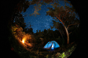 Modern camping tent and bonfire in forest at night. Fisheye lens effect