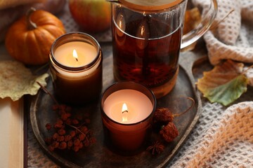 Burning candles, freshly brewed tea and autumn decor on fabric, closeup