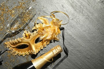 Beautiful golden carnival mask, bottle of sparkling wine, glass and confetti on gray textured...