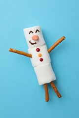 Funny snowman made of marshmallows on light blue background, top view