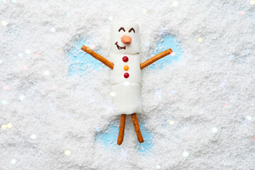 Marshmallow snowman making angel on artificial snow, top view