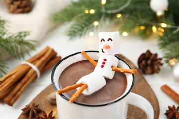 Funny snowman made with marshmallows in cup of hot chocolate and winter decor on white table, closeup