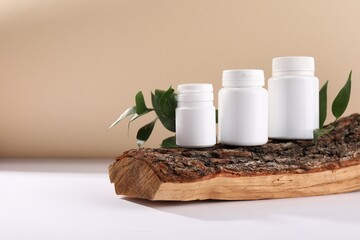 Plastic medical bottles, green leaves and snag on white table