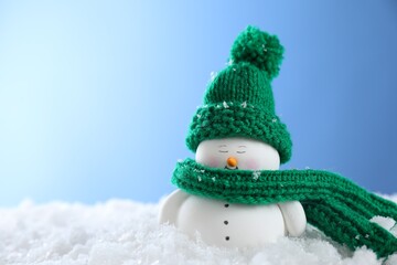 Cute decorative snowman on artificial snow against light blue background. Space for text
