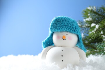 Cute decorative snowman on artificial snow against light blue background. Space for text