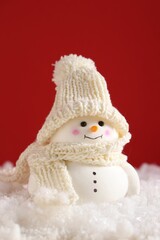 Cute decorative snowman on artificial snow against red background