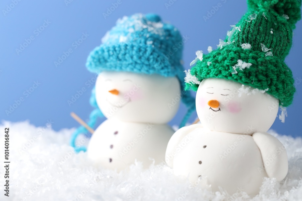 Poster Cute decorative snowmen on artificial snow against light blue background, closeup