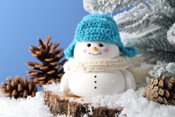 Cute decorative snowman, fir tree branches and cones on artificial snow against light blue background, closeup