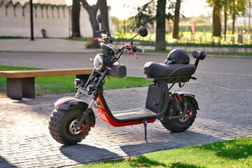 Modern red electric scooter with helmet on seat in city.