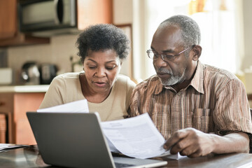 Obraz premium Senior couple reviewing financial documents together on a laptop, symbolizing retirement planning and budgeting. 