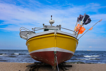 A small fishing boat standing on the beach on the seashore against the sky background.