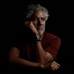 Low key, high contrast color portrait of an attractive older Caucasian man with grey hair and beard. Looking to the left with serious or pensive expression.  