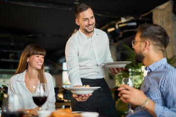 Mid adult waiter serving group of business people during lunch time in a restaurant.