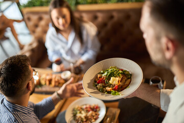 Close up of unrecognizable man holding plate with food while serving group of business people during lunch time in a restaurant. Focus is on a plate.