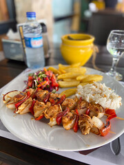 Delicious plate of grilled chicken skewers with rice, salad, and fries on a wooden table setting. Well-balanced and colorful meal, perfect for a vibrant dining experience