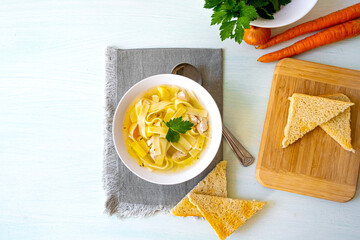 Chicken soup with noodles and vegetables in white bowl