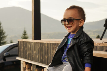 Casual handsome boy wearing leather jacket and sunglasses sitting outdoor