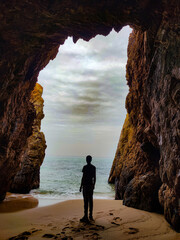 the silhouette of a man from behind standing at the exit of a cave by the sea, and looking towards...