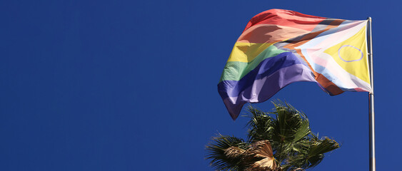 Intersex-inclusive redesign of the Progress Pride Flag. Rainbow LGBT flag against a blue sky. Flag...